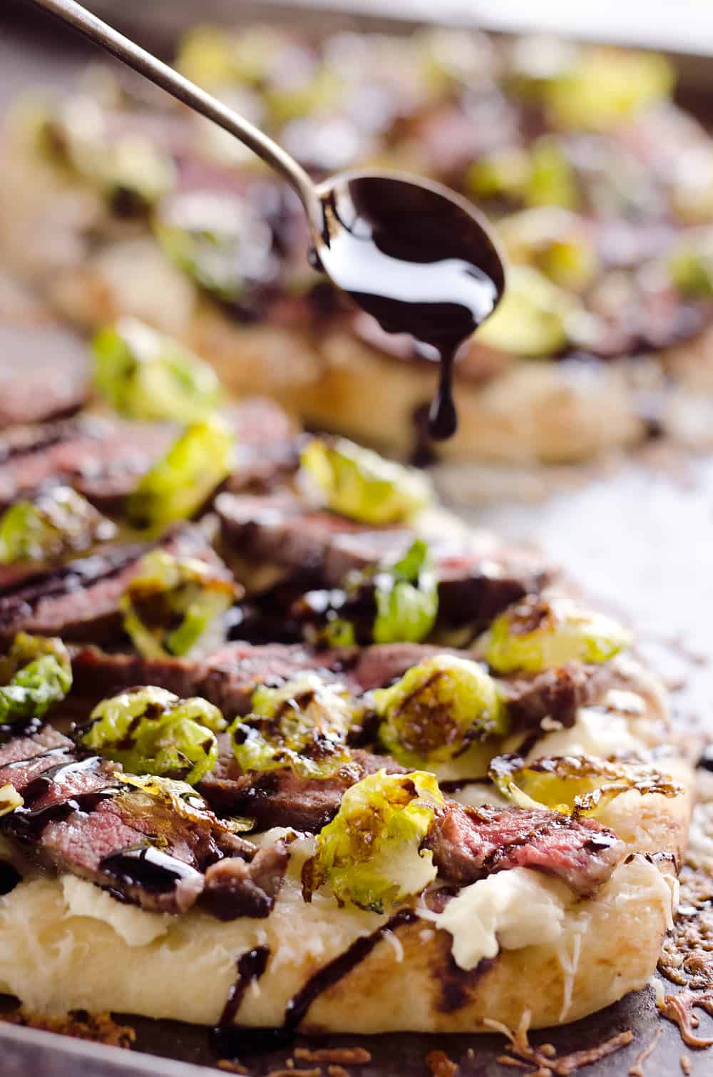 Steak, Goat Cheese & Roasted Brussels Sprout Flatbread is a hearty dinner idea bursting with bold flavors. A chewy naan bread is topped with goat cheese, grilled steak, roasted brussels sprout leaves and a balsamic glaze for a delicious and unique recipe you will make again and again!