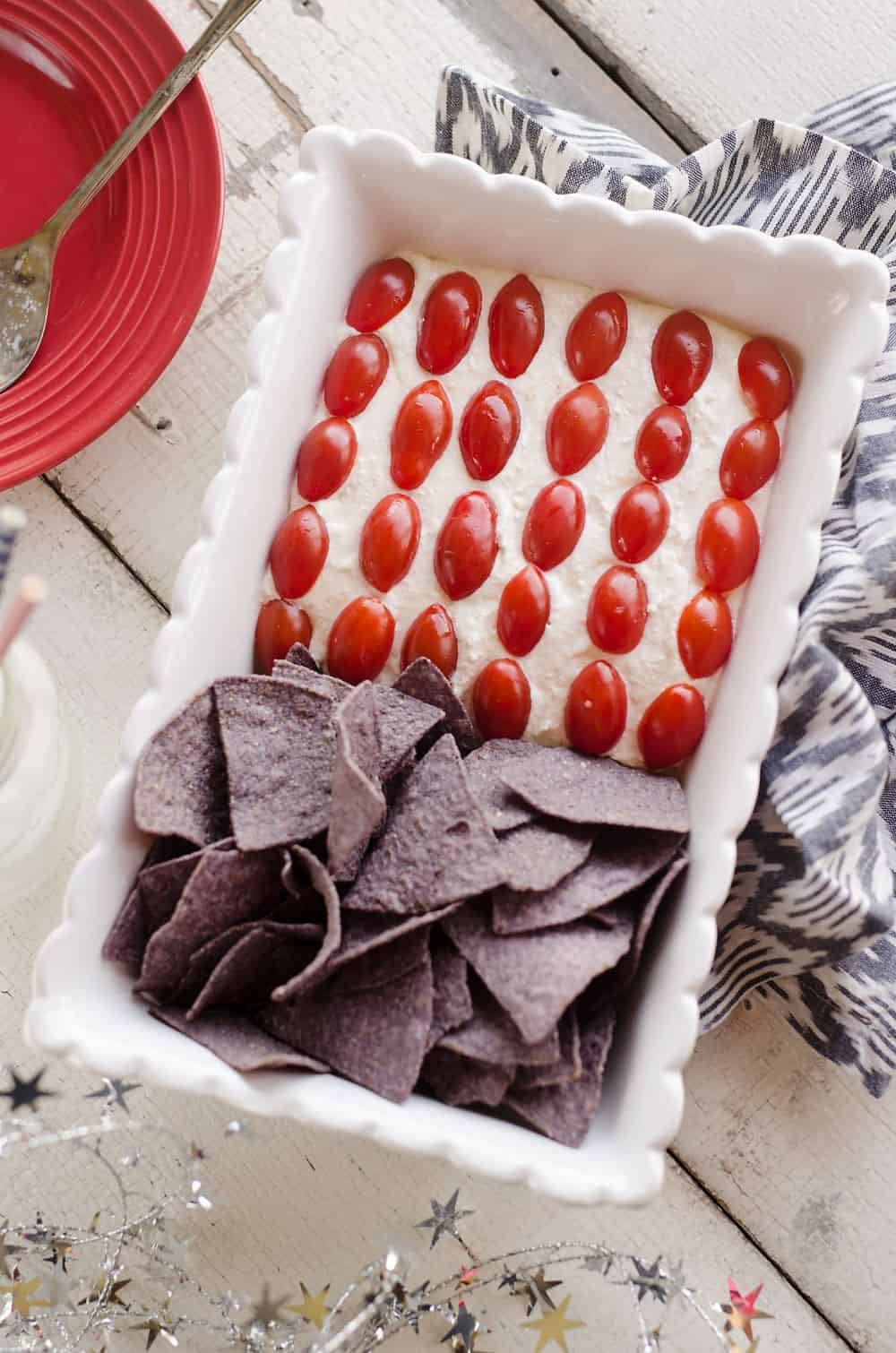 Patriotic Flag Parmesan Garlic Chip Dip is a festive appetizer recipe perfect for a holiday party with red, white and blue colors! A creamy Parmesan garlic dip is topped with cherry tomatoes and served with blue corn tortilla chips for a delicious dish sure to be a crowd pleaser.