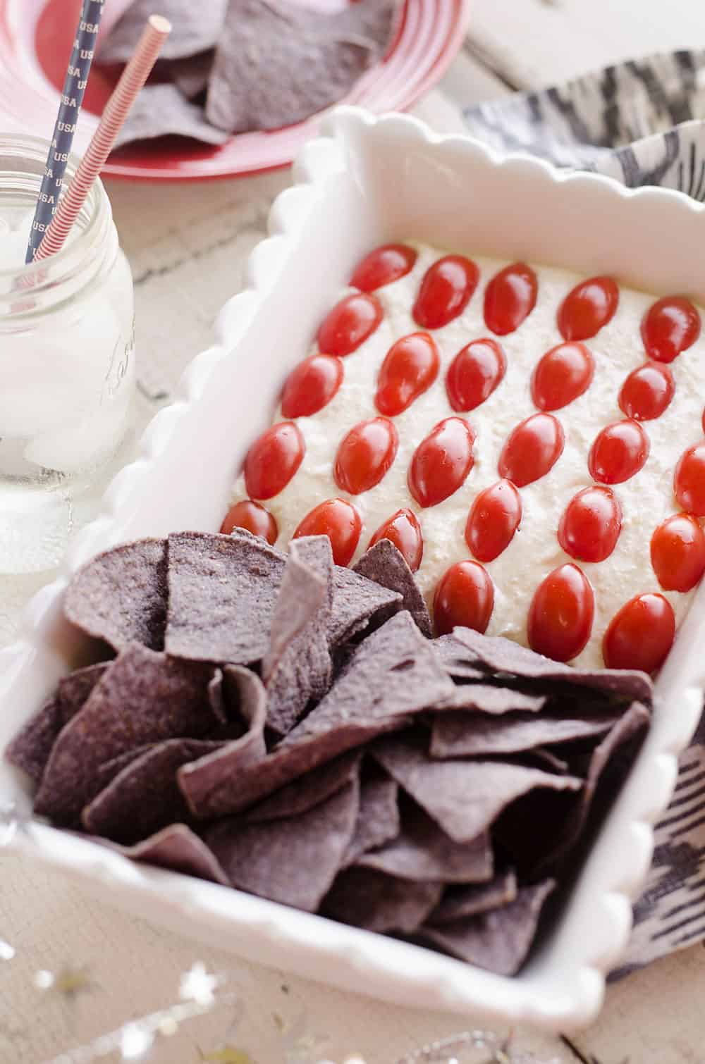 Patriotic Flag Parmesan Garlic Chip Dip is a festive appetizer recipe perfect for a holiday party with red, white and blue colors! A creamy Parmesan garlic dip is topped with cherry tomatoes and served with blue corn tortilla chips for a delicious dish sure to be a crowd pleaser.